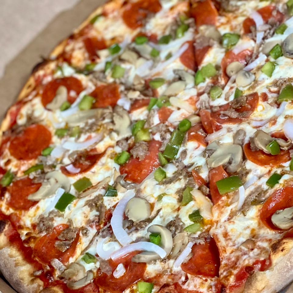 A close-up of a Sam's NY Pizza pie with pepperoni, sausage, mushrooms, green peppers, and onions.