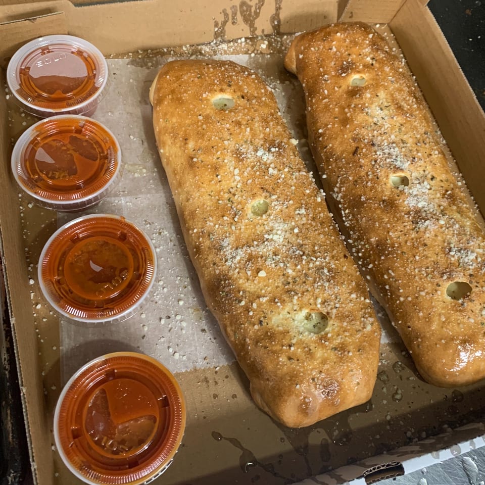 Two golden-brown calzones, sprinkled with parmesan and herbs, in a pizza box with four cups of marinara.