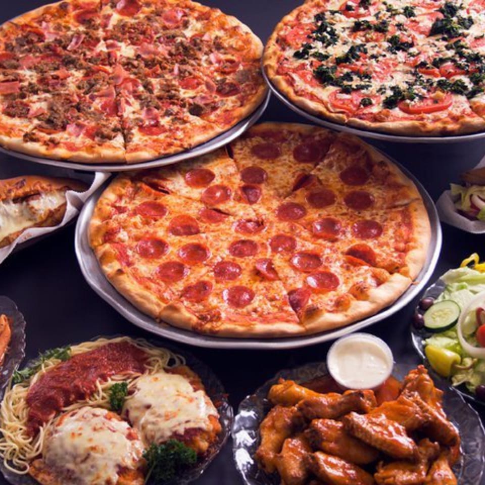A feast of Sam's NY Pizza, including pepperoni, meat, and veggie pizzas, wings, pasta, and salad.